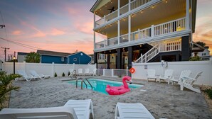 Ein Poolbereich mit Liegestühlen, einem Flamingo-Schwimmpfad und einem zweistöckigen Gebäude mit Balkonen.