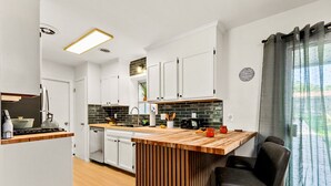 Una cocina moderna con armarios blancos, encimera de madera y salpicadero de baldosas negras.