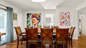 Un comedor con una mesa y sillas de madera, una lámpara de techo y dos cuadros grandes en las paredes.