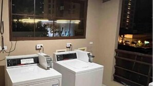 A laundry room with two washing machines, a window, and a view of the city at night.