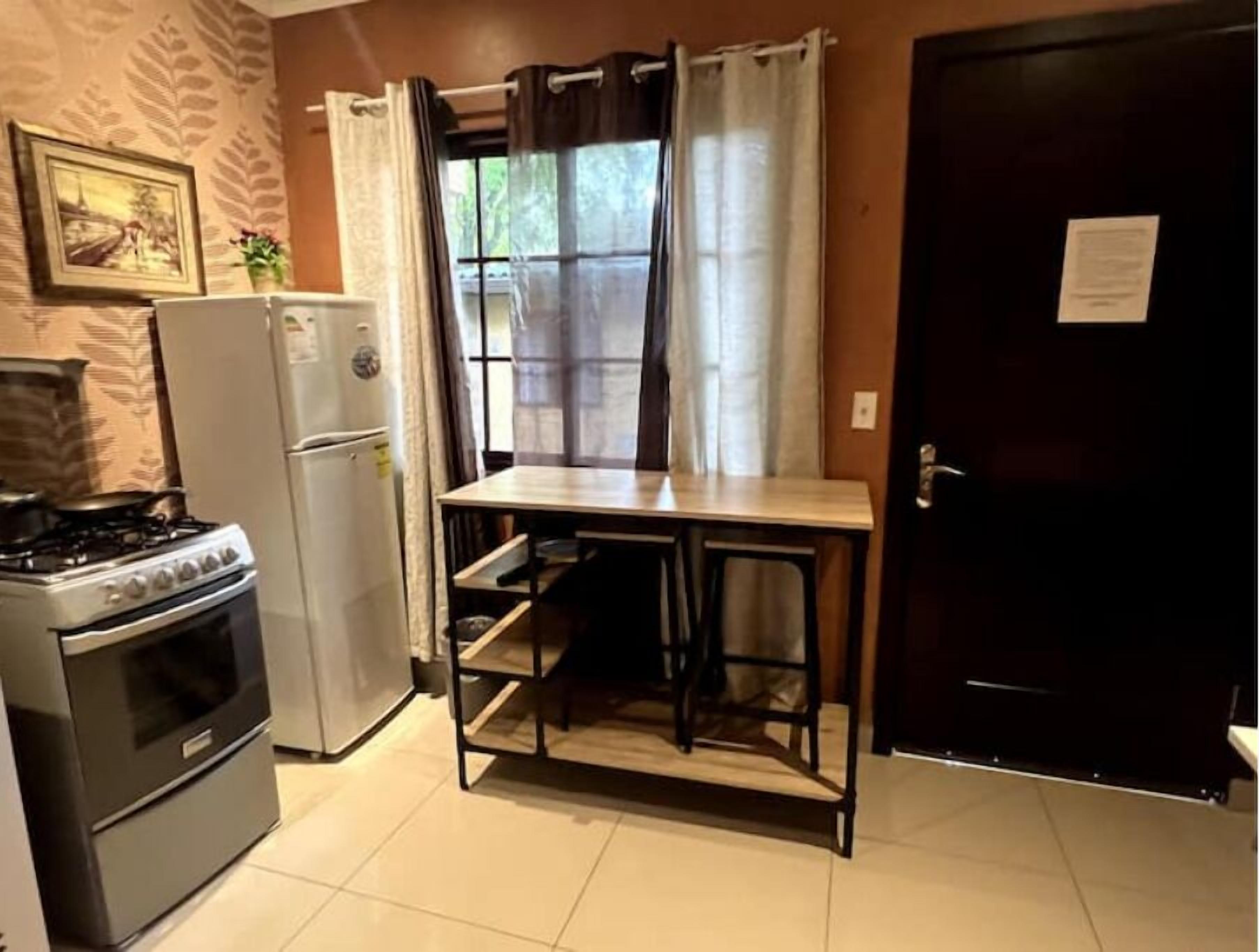 A compact kitchen with a stove, refrigerator, and a small table with shelves.