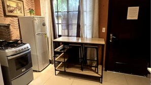 A compact kitchen with a stove, refrigerator, and a small table with shelves.