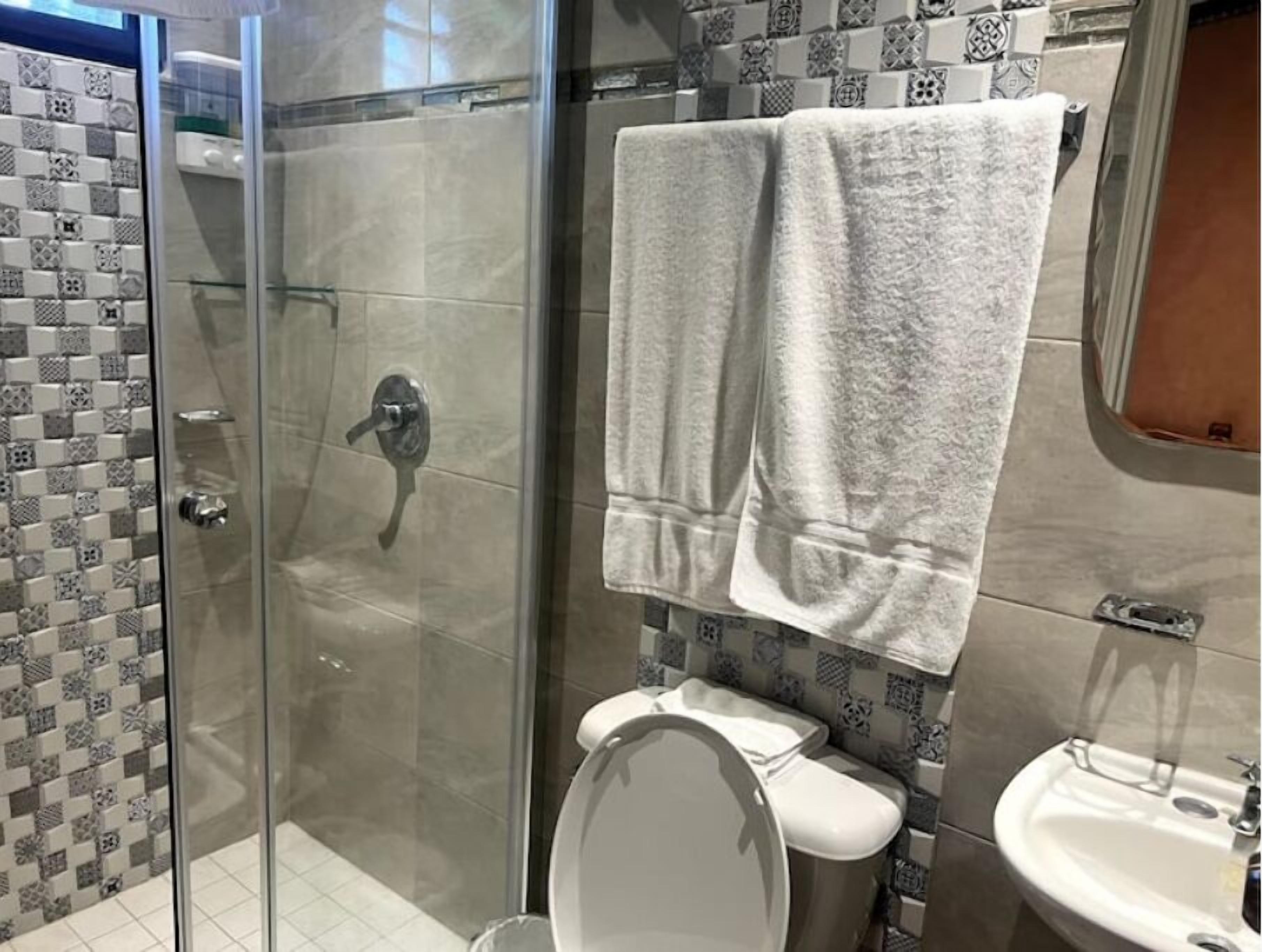 A bathroom with a glass shower enclosure, a toilet, and a sink.