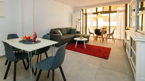 Una sala de estar moderna con comedor, un sofá, un ventilador de techo y vistas amplias por ventanas grandes.