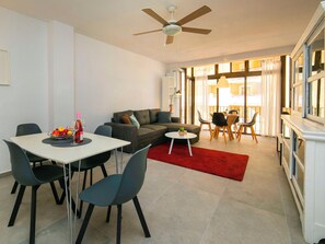 A modern living room with a dining area, a sofa, a ceiling fan, and a view through large windows.
