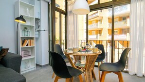 Una sala de estar moderna con una mesa de comedor redonda, sillas negras, una lámpara colgante blanca y vistas a un balcón con barandilla.