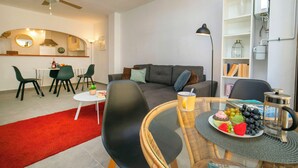 Una sala de estar moderna con sofá, mesa de comedor, sillas y una zona de cocina al fondo.