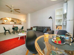 A modern living room with a sofa, dining table, chairs, and a kitchen area in the background.