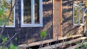En stuga med en träfasad, en ytterdörr och en liten veranda.