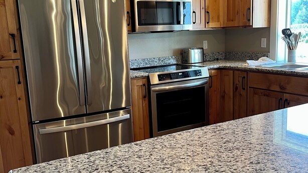 A kitchen with wooden cabinets, stainless steel appliances, granite countertops, and a window with a view.