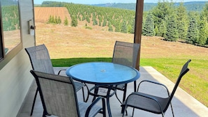 A covered patio with a round table and four chairs, overlooking a forested landscape.