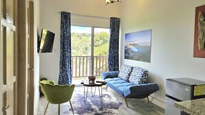 A living room with a sofa, a green chair, a small table, and a refrigerator. - Charming chalet with WiFi in Poas. Great trails, and pools (Poas)