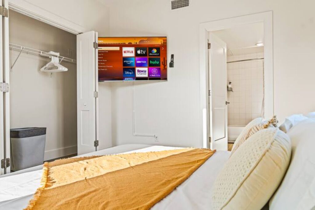 Une chambre d’hôtel comprenant un lit, un téléviseur fixé au mur diffusant divers services de streaming, un placard avec une tringle pour suspendre les vêtements, et une salle de bain visible à travers une porte ouverte.