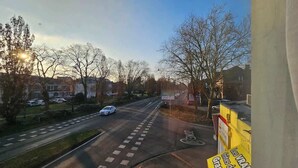 Eine Straße mit einem weißen Auto, Bäumen und Gebäuden im Hintergrund.