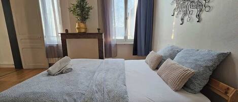 A bedroom with a bed, pillows, a bedside table with a plant, and a wall decoration.