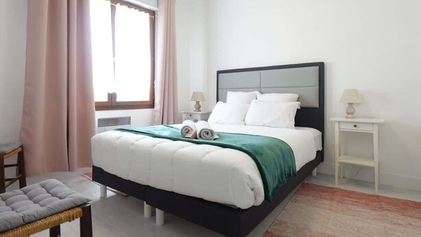 A neatly arranged bedroom with a bed, bedside tables, and a chair. - Le Carvinois, wifi, Carvin centre, 2pers (Carvin)