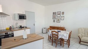 A compact kitchen with a microwave, sink, and stove. There is a dining area with a table and chairs. - Le Carvinois, wifi, Carvin centre, 2pers (Carvin)