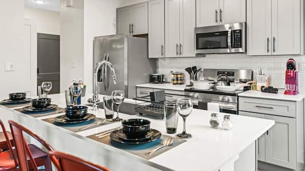 A modern kitchen with white cabinets, stainless steel appliances, and a dining area set with plates, glasses, and cutlery.