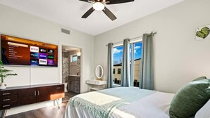 Une chambre à coucher comprenant un lit, une commode, un téléviseur fixé au mur qui permet d’accéder à des services de diffusion en continu, et une fenêtre avec des rideaux.