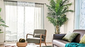 Un salon avec un canapé, un fauteuil et une grande plante en pot.