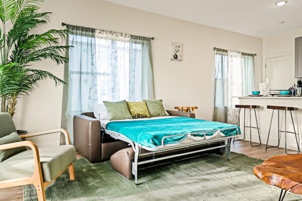 A bedroom with a bed, a chair, a desk, and a plant.