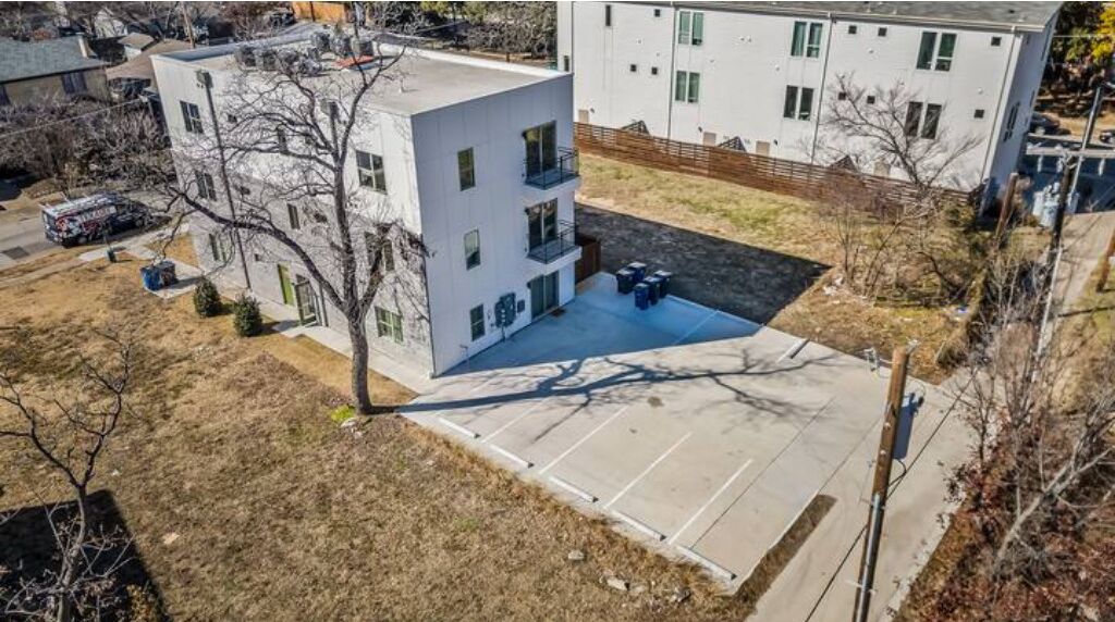 A multi-story building with a flat roof, a parking area, and a small garden.
