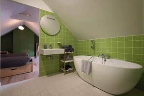 Ein Schlafzimmer mit Bett, ein Badezimmer mit Badewanne und einer grün gefliesten Wand.