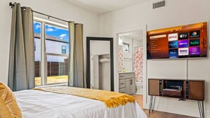 Une chambre à coucher avec un lit, un téléviseur fixé au mur qui diffuse des services de streaming, et un petit meuble placé sous le téléviseur.