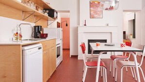 Une cuisine moderne avec des appareils électroménagers blancs, un coin repas avec des chaises rouges et une cheminée.