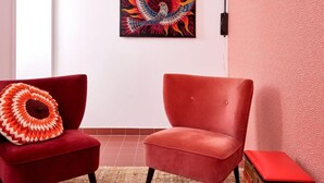 Un salon moderne avec un fauteuil en velours rouge, un pouf assorti et un tableau abstrait aux couleurs vives accroché au mur.