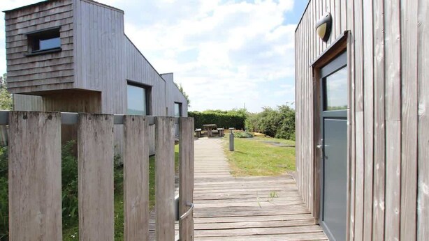 Una terraza de madera que conduce a un edificio moderno con una puerta y una ventana.