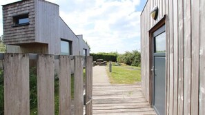 A wooden deck leading to a modern building with a door and window. - Les écolodges, Site Eco Naturel, 8 pers (Mont-Bernanchon)
