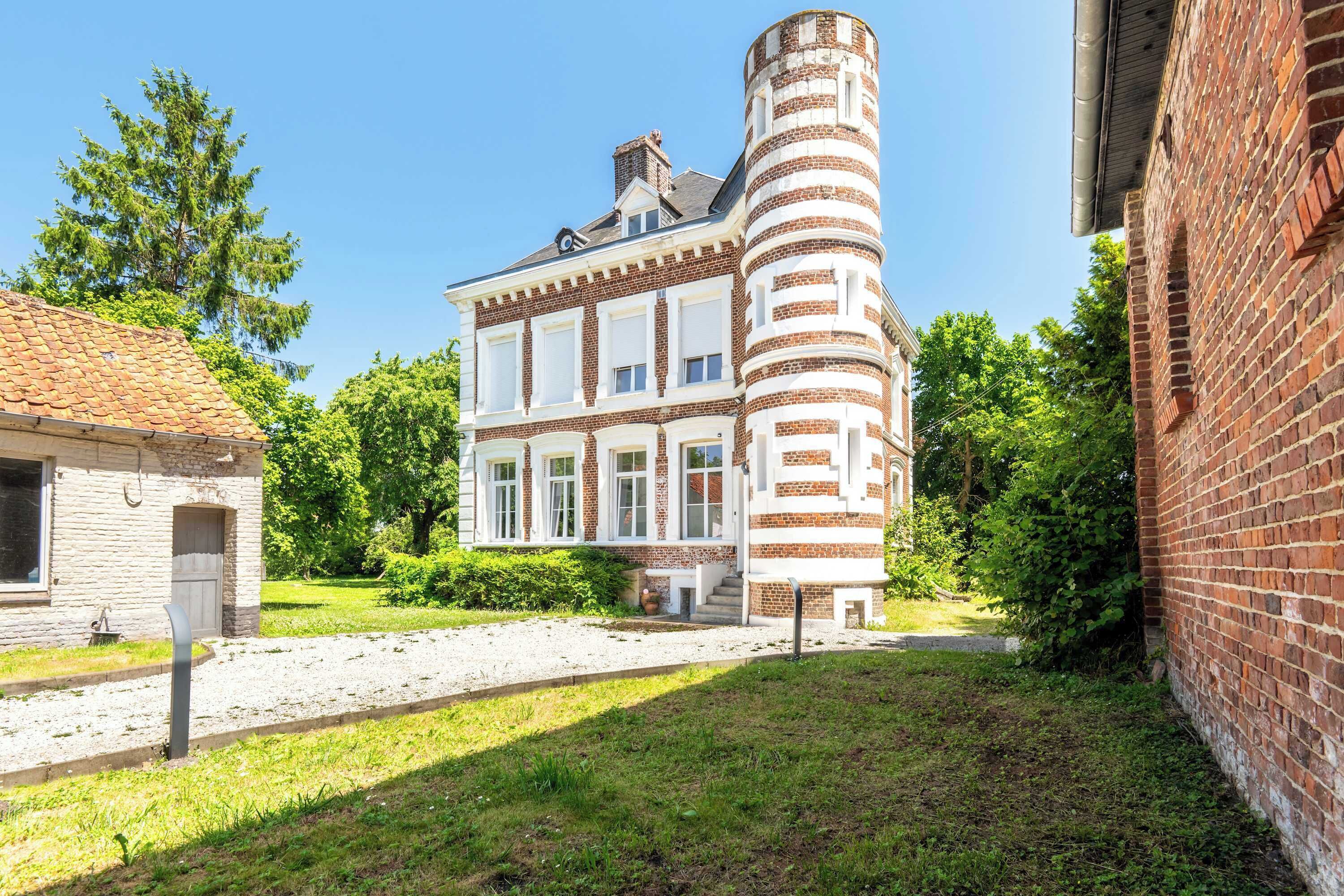 Un bâtiment à deux étages, doté d’une façade en briques et d’une tour distinctive aux rayures blanches et rouges.