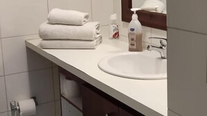 Ein Badezimmer mit einem weißen Waschbecken, einem Spiegel und einem Stapel Handtüchern.