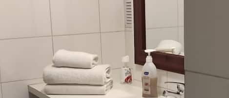 Un baño con un lavamanos blanco, un espejo y una pila de toallas.