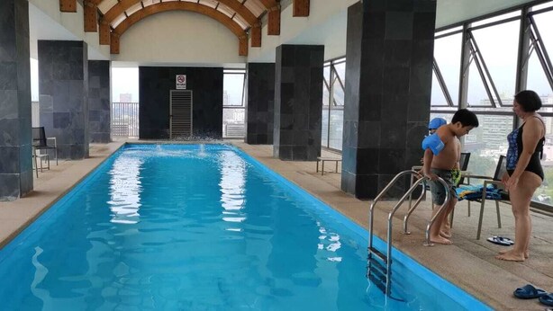 Ein Hallenbad mit Blick auf die Skyline der Stadt, ein Sprungverbotsschild und ein Rettungsschwimmerstuhl.
