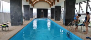 An indoor swimming pool with a view of the city skyline, a no diving sign, and a lifeguard chair. - ARTE CENTRO (Santiago)