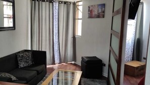 Ein Wohnzimmer mit einer schwarzen Couch, einem Glastisch, einem schwarzen Hocker und einem gerahmten Spiegel an der Wand.