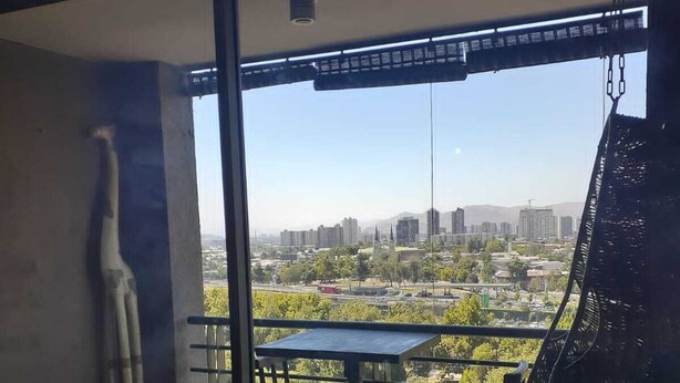 A balcony with a view of a cityscape, a hanging chair, and a potted plant. - Centro wifi vista despejada (Santiago)