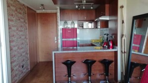 A compact kitchen with a central island, three bar stools, and wooden cabinets. - Centro wifi vista despejada (Santiago)