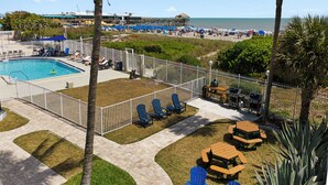 A pool area with lounge chairs, a barbecue setup, and a view of the beach. - Nice and Beautiful Unit - Oceanfront Condo Pool near Attractions (Cocoa Beach)