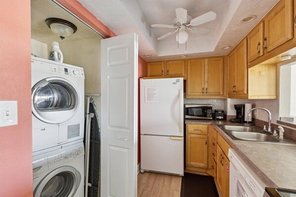 A compact kitchen with a washing machine, a refrigerator, and wooden cabinets.