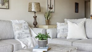 A living room with a grey sofa, a coffee table with a book and a plant, a lamp, and a wall with an anchor decoration. - Nice and Beautiful Unit - Oceanfront Condo Pool near Attractions (Cocoa Beach)
