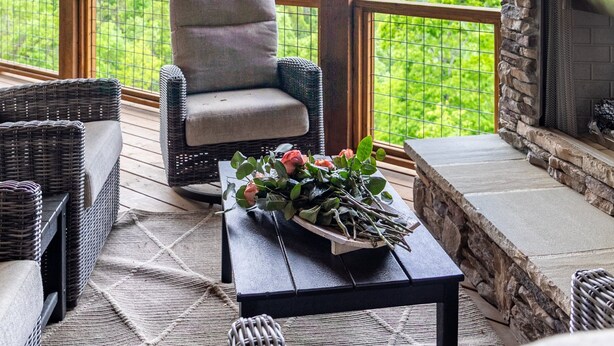 A covered outdoor seating area with wicker furniture, a stone fireplace, and a view of green hills.