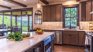 A modern kitchen with dark wooden cabinets, a marble countertop, and a large window offering a view of greenery.