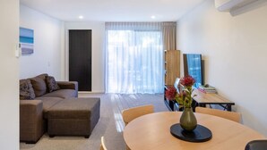 A modern living room with a sofa, ottoman, and a dining table with chairs.