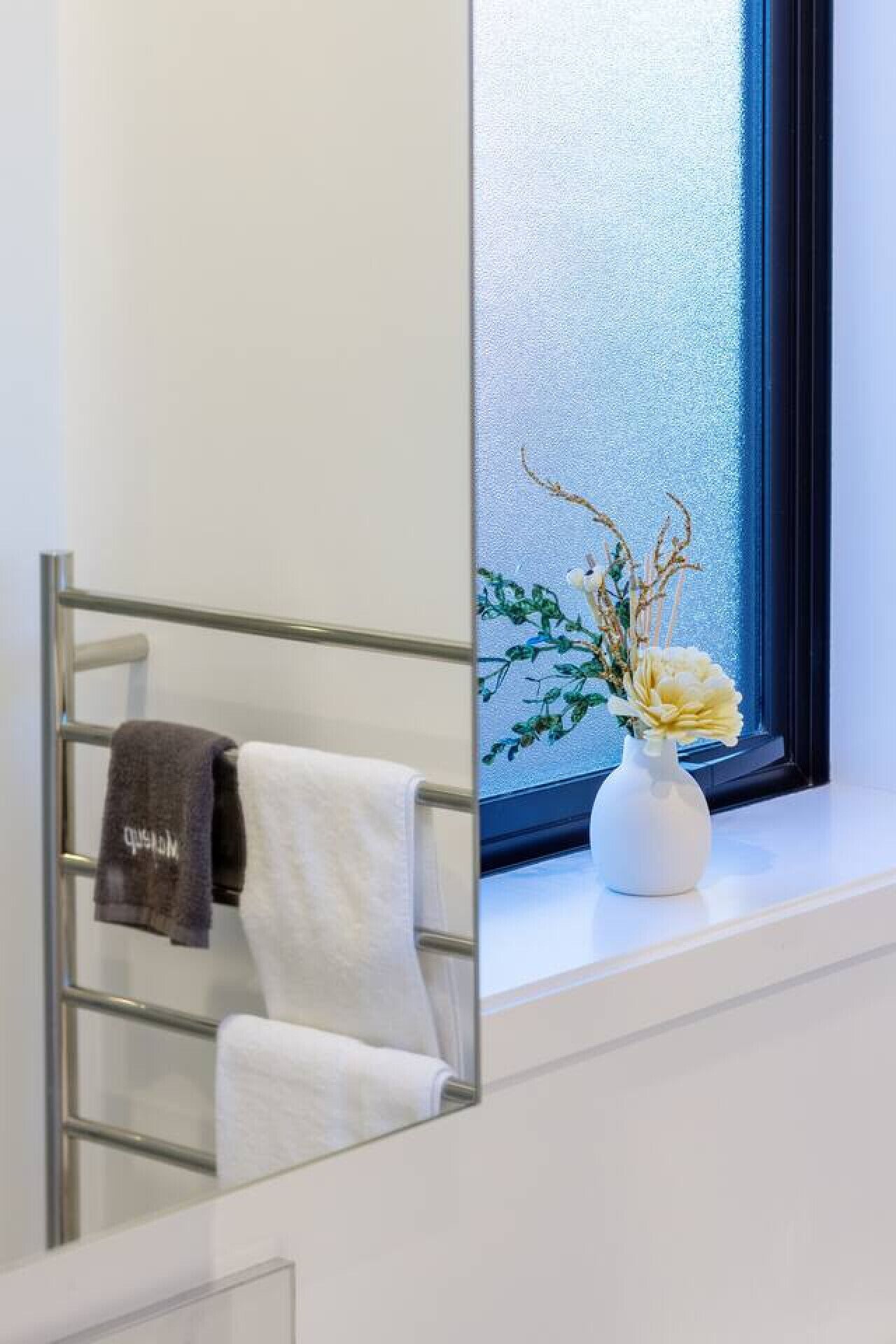 Un baño con un toallero que sostiene dos toallas, una ventana con vista al exterior y un florero con flores en el alféizar.