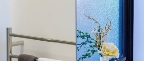 Un baño con un toallero que sostiene dos toallas, una ventana con vista al exterior y un florero con flores en el alféizar.
