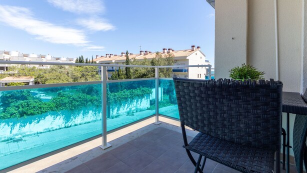 Un balcón con vistas despejadas a una piscina, una silla de mimbre y una planta en maceta.