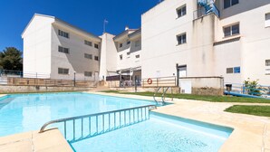 Una piscina con una escalera metálica, rodeada por un borde de hormigón. Se observan edificios con múltiples ventanas y balcones al fondo.